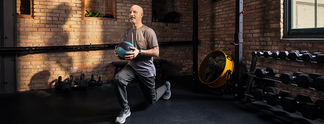 Image of male hearing aid wearer doing forward lunges in the gym with a ball in hand